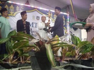 Kepala Desa Pengenjek menyerahkan tropi juara umum MTQ Tingkat Desa ke-XXX.